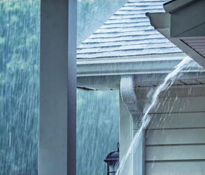 Heavy rain falling on house roof overflowing gutters