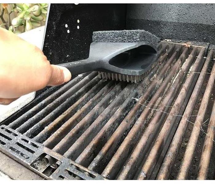 Gas grill grates being cleaned with a long handle wire brush